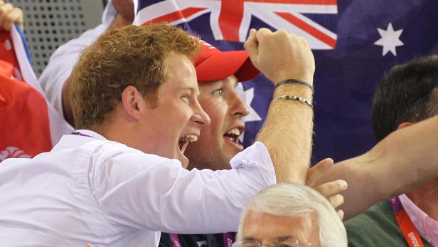 Prinz Harry jubelt mit einem Mann im roten Hut vor einer australischen Flagge.