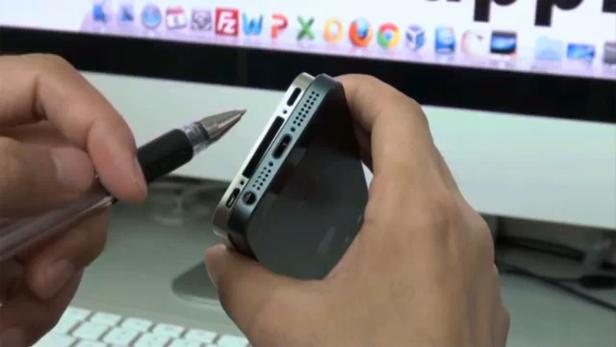 Eine Person hält ein iPhone und einen Stift vor einem Computerbildschirm.
