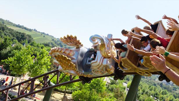 Menschen fahren mit einer Achterbahn im Themenpark bei strahlendem Sonnenschein.