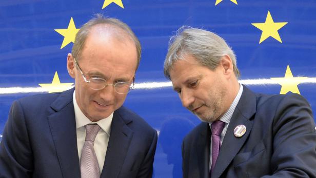 Zwei Männer in Anzügen stehen vor einer EU-Flagge.
