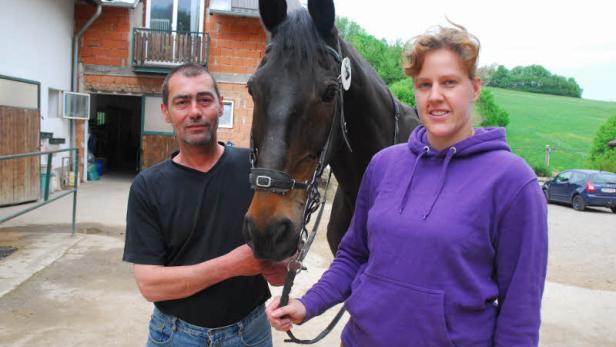 Ein Mann und eine Frau stehen mit einem dunklen Pferd vor einem Haus.