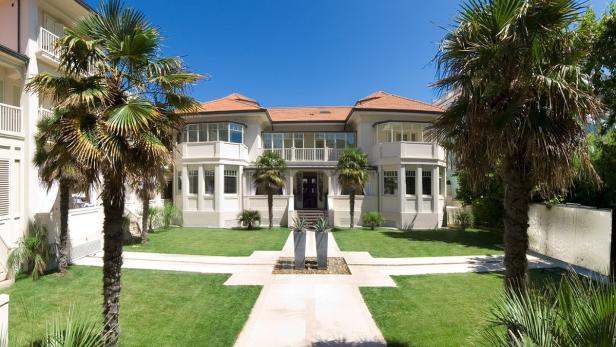 Ein zweistöckiges, helles Gebäude mit einem roten Ziegeldach und Palmen im Garten.