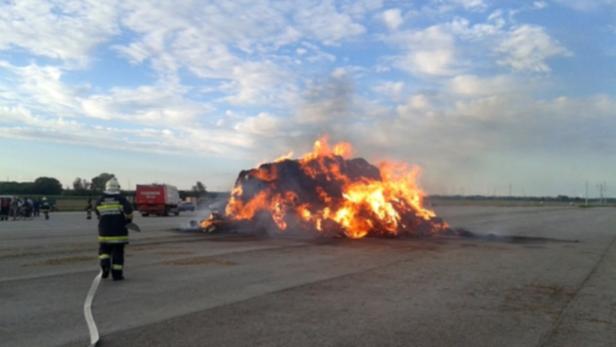 Ein Feuerwehrmann steht vor einem brennenden Heuhaufen.