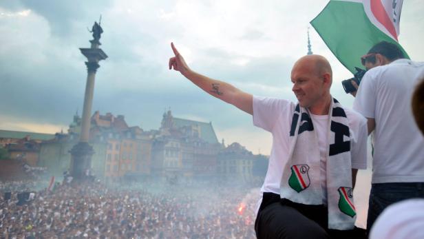 Ein Mann mit Legia-Warschau-Schal steht vor einer Menschenmenge in Warschau.