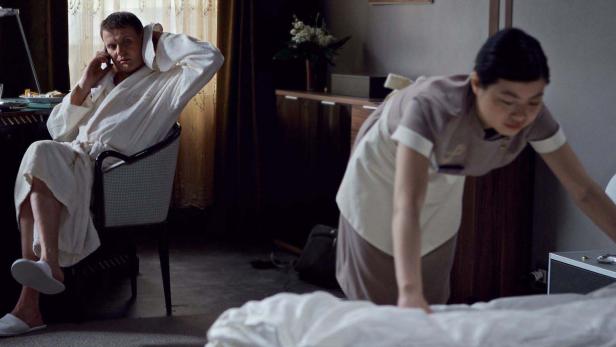 Ein Mann im Bademantel telefoniert, während ein Zimmermädchen das Bett macht.