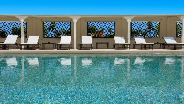 Mehrere Liegestühle stehen am Rande eines türkisfarbenen Pools.