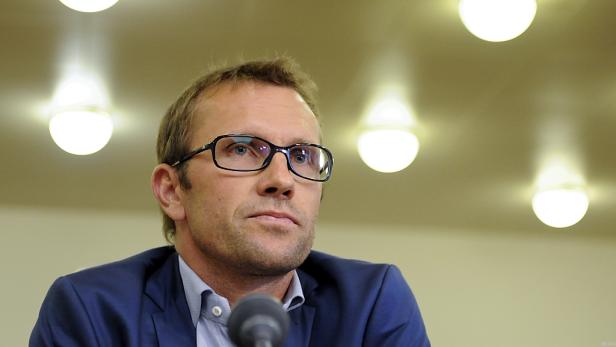 Ein Mann mit Brille und blauem Sakko steht vor einem Mikrofon.