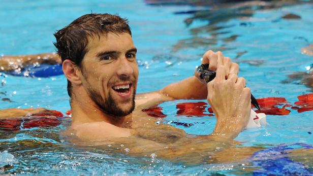 Michael Phelps lächelt im Schwimmbecken und hält seine Schwimmbrille in der Hand.