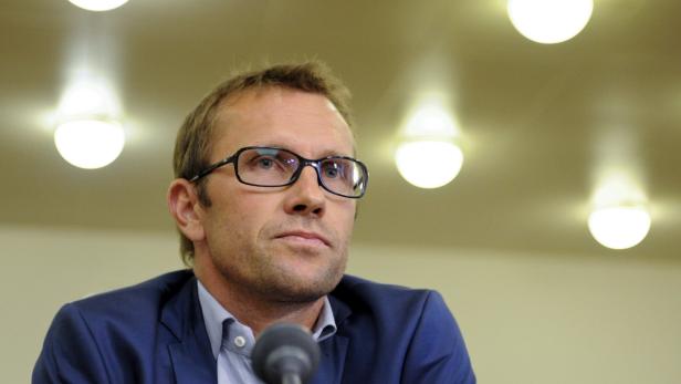 Ein Mann mit Brille und blauem Sakko spricht in ein Mikrofon.