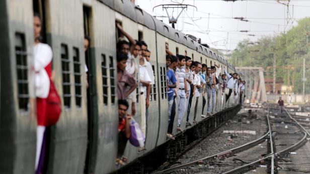 Ein überfüllter Zug in Indien mit Menschen, die aus den Türen schauen.