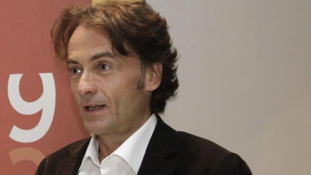 Ein Mann mit braunen Haaren und einem dunklen Jackett spricht.