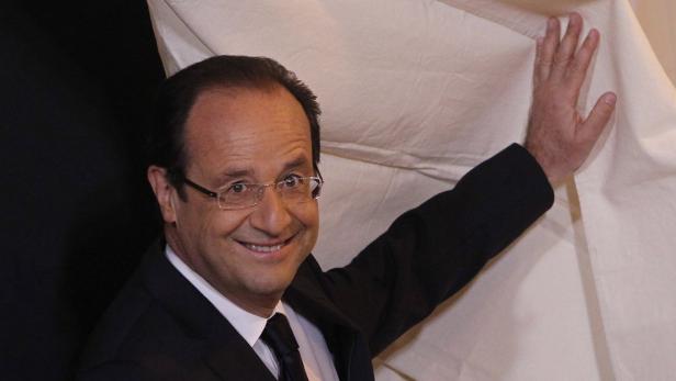 François Hollande lächelt, während er ein Tuch zur Seite zieht.