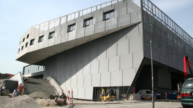 Bauarbeiten vor einem modernen, grauen Gebäude mit ungewöhnlicher Architektur.