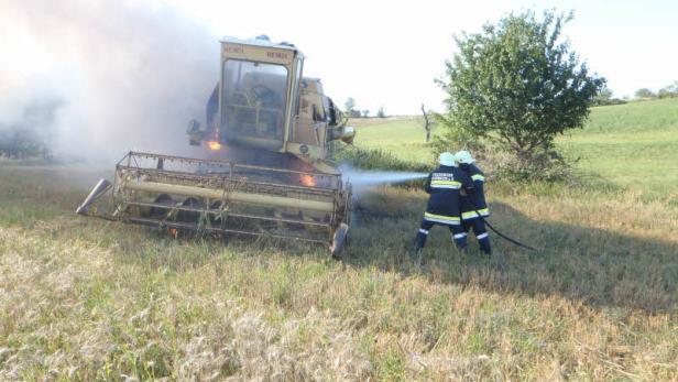 Zwei Feuerwehrleute löschen einen brennenden Mähdrescher auf einem Feld.