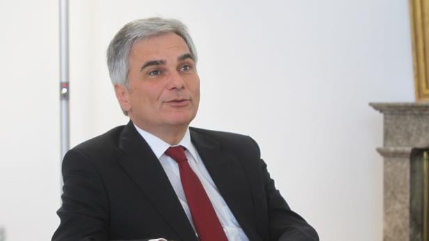 Ein Mann mit grauem Haar, Anzug und roter Krawatte sitzt in einem Raum.