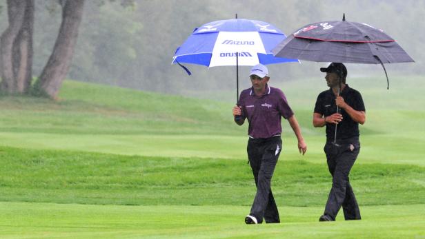 Zwei Golfer gehen mit Schirmen bei Regen über einen Golfplatz.