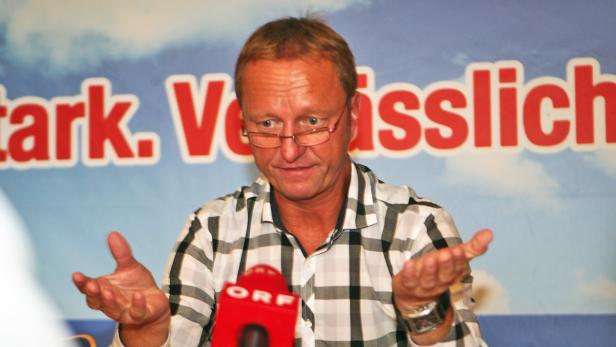 Ein Mann mit Brille gestikuliert vor einem Mikrofon des ORF.