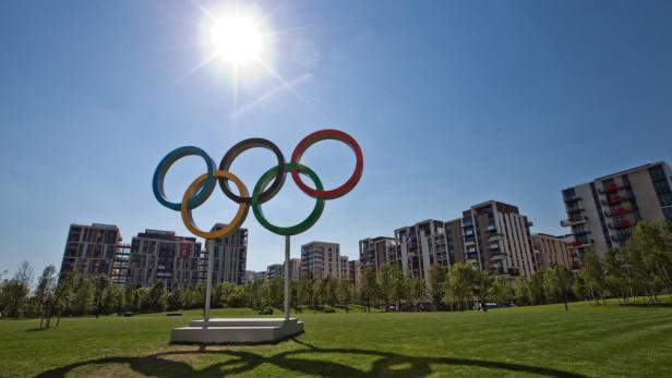 Die olympischen Ringe stehen in einem Park vor Wohngebäuden.