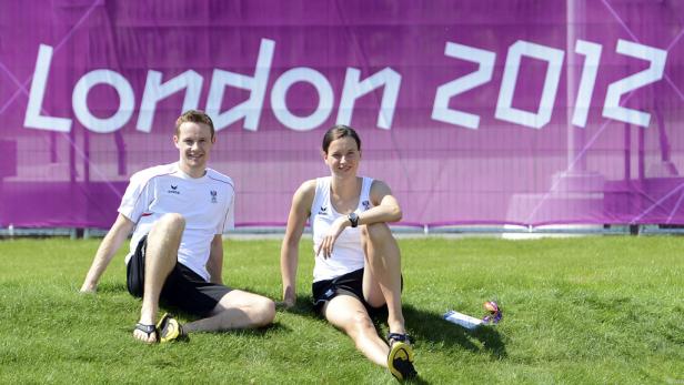 Zwei österreichische Athleten sitzen vor einem „London 2012“-Banner auf einer Wiese.