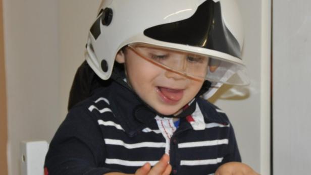 Ein kleiner Junge trägt einen Feuerwehrhelm und spielt an einem Tisch.