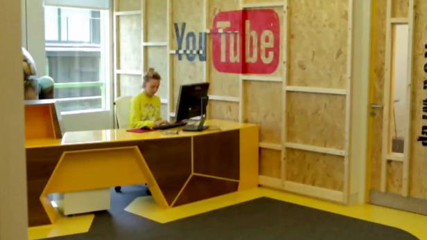 Eine junge Frau arbeitet an einem Computer in einem Büro mit YouTube-Logo.