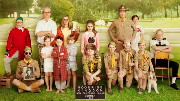 Eine Gruppenaufnahme der Besetzung des Films „Moonrise Kingdom“ vor einem gemalten Hintergrund.