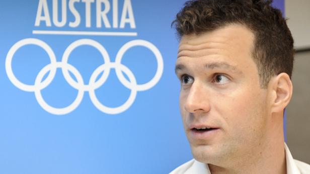 Ein Mann steht vor einem blauen Hintergrund mit dem Logo des österreichischen Olympischen Komitees.