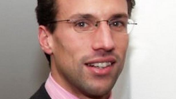 Ein Mann mit Brille, Anzug und gestreifter Krawatte lächelt.