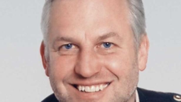 Ein lächelnder Mann mit grauen Haaren und blauen Augen vor einem hellen Hintergrund.
