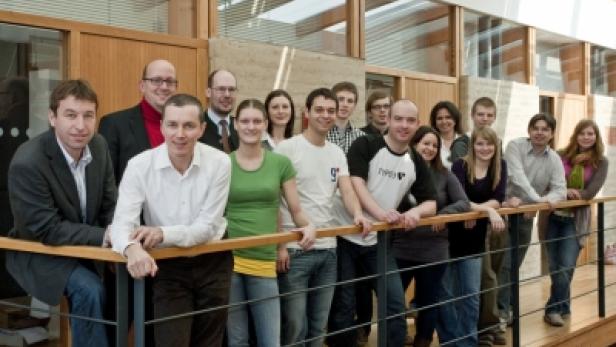 Eine Gruppe von etwa 15 Personen posiert auf einer Galerie für ein Foto.
