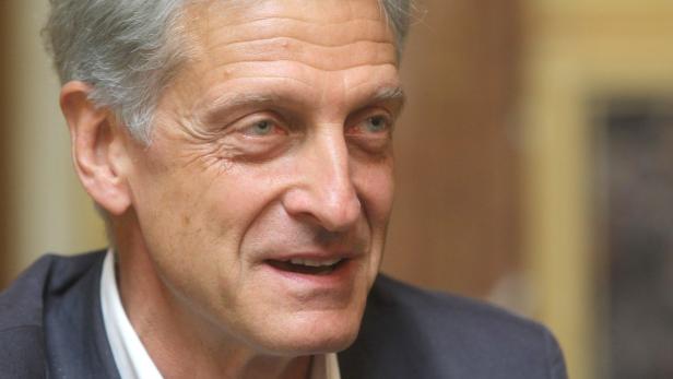 Porträt eines Mannes mit grauen Haaren und einem dunklen Anzug.