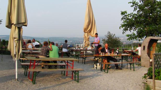 Menschen sitzen an Tischen im Freien mit Blick auf eine Stadt.