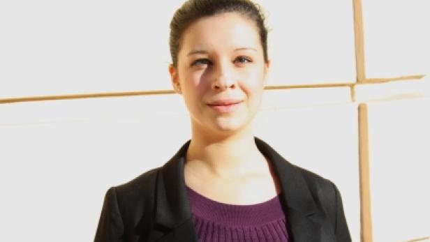 Eine junge Frau mit dunklen Haaren und einem schwarzen Blazer lächelt in die Kamera.