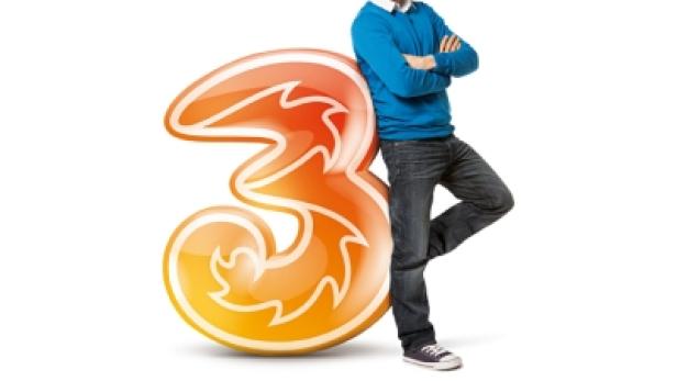 Ein Mann lehnt an einem großen, orangefarbenen Logo der Mobilfunkmarke Drei.