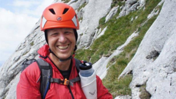 Vermisster am Untersberg Salzburg… Ein lächelnder Mann mit roter Jacke und Helm steht vor einem felsigen Berghang.