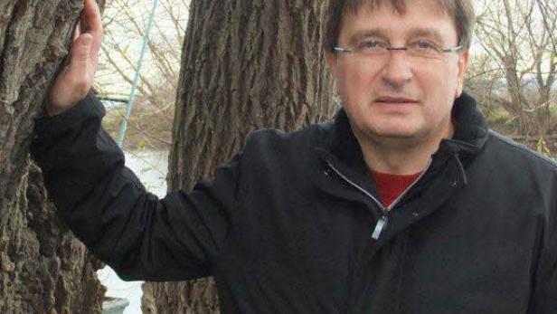 Ein Mann mit Brille lehnt an einem Baum im Freien.