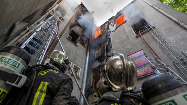 Feuerwehrleute stehen vor einem brennenden Gebäude.