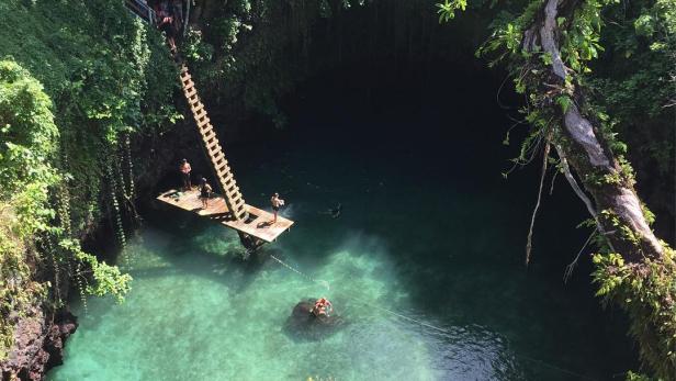 Menschen schwimmen in einem natürlichen Pool mit einer Plattform und einer Leiter.
