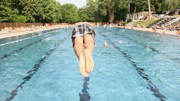 Ein Mann springt mit dem Kopf voran in ein Schwimmbecken voller Menschen.