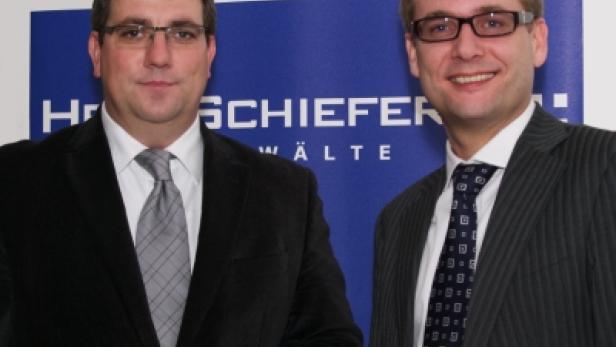 Zwei Männer in Anzügen stehen vor einem blauen Banner der Kanzlei Harschiesiefer & Wälte.