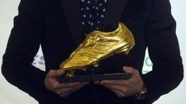Eine Person im Anzug hält einen goldenen Fußballschuh-Pokal.