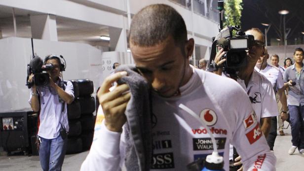 Lewis Hamilton wischt sich mit einem Handtuch das Gesicht, umringt von Kameraleuten.