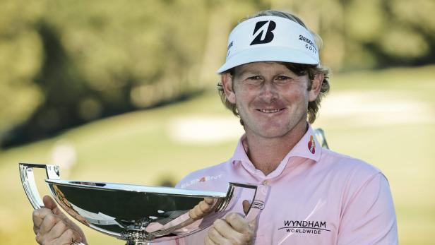 Ein lächelnder Golfer hält eine silberne Trophäe in den Händen.