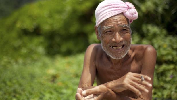 Ein älterer Mann mit einem rosa Turban raucht eine Zigarette.