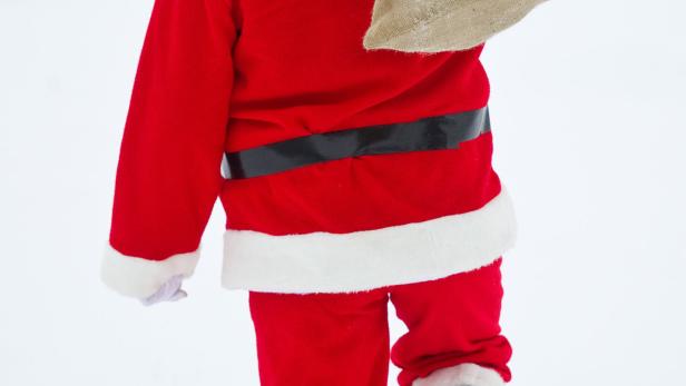 Der Weihnachtsmann geht mit einem Sack über der Schulter durch den Schnee.
