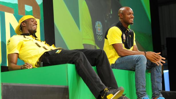 Usain Bolt und ein weiterer Mann sitzen auf einer Bühne und lächeln.