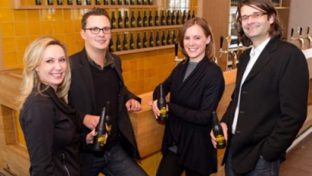 Vier Personen stehen in einer Bar und halten Bierflaschen in der Hand.