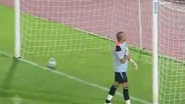 Ein Torwart steht neben einem Fußballtor auf einem grünen Rasen.