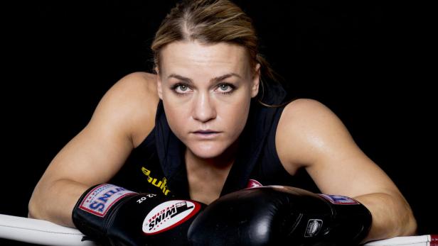 Eine Boxerin mit Boxhandschuhen lehnt im Ring.