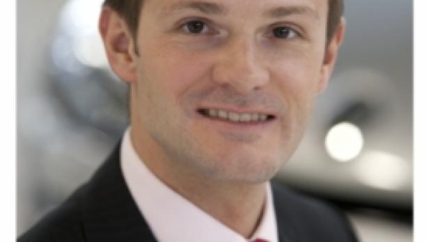 Ein Mann mit dunklen Haaren und roter Krawatte lächelt in die Kamera.